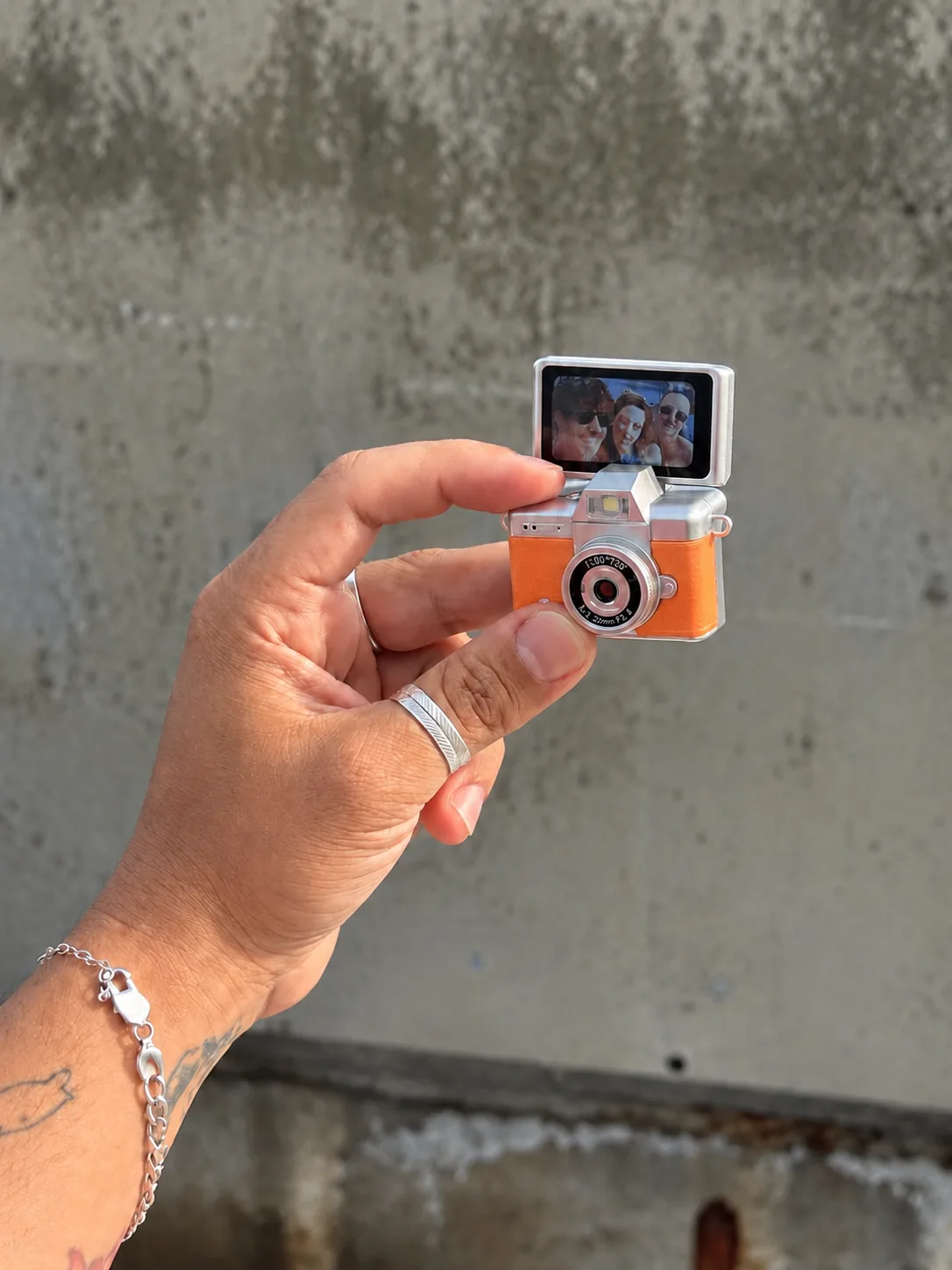 Mano sujetando la Cámara Mini naranja con la pantalla abierta 180°, mostrando a tres personas en el encuadre